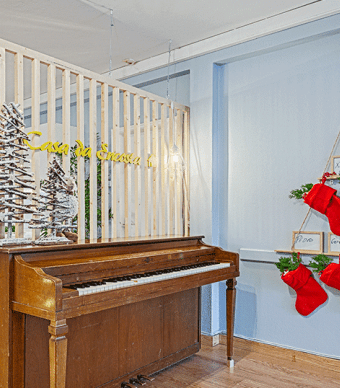 Sala de estar com uma árvore de natal na parede, um piano no centro, decorações de Natal, mesas de cozinha e cadeiras